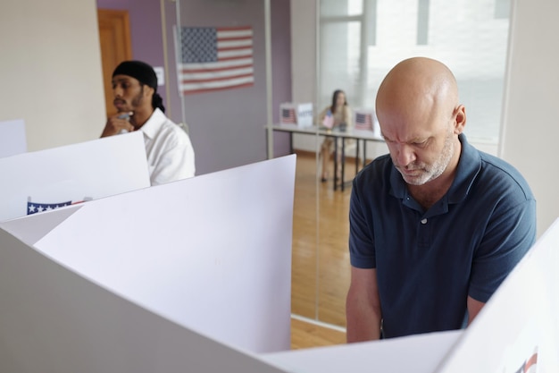 A close-up photo of a voter placing their completed ballot into an early voting ballot box. The ballot box looks secure and official, with a clear indication of its purpose.