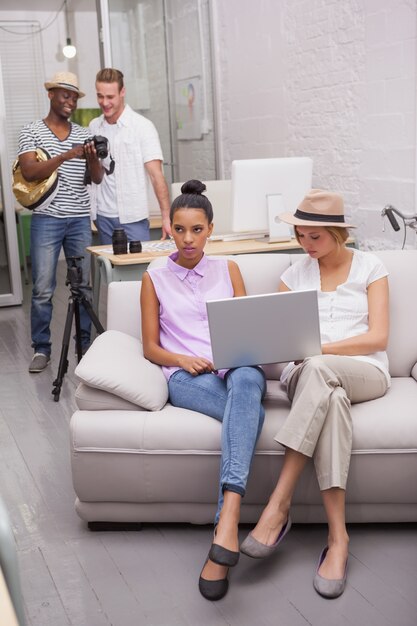 An eye-level shot of a diverse group of people using laptops and smartphones to research voting information online. The scene takes place in a modern co-working space.
