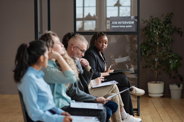 A diverse group of people engaged in a town hall meeting, listening attentively to a speaker presenting policy proposals on a screen.