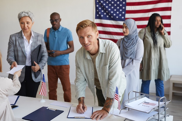 A diverse group of election officials counting ballots at a table with stacks of paperwork and computers.
