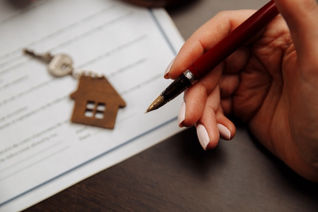 A close-up shot of a hand signing mortgage documents, with a house key lying on top of the papers. The image highlights the intricacies of the home buying process and the importance of understanding policy changes.