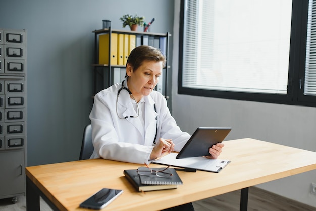 A doctor sitting at a desk in a well-lit office, reviewing documents related to telehealth regulations on a tablet. The scene showcases the administrative and compliance aspects of telehealth for healthcare professionals.