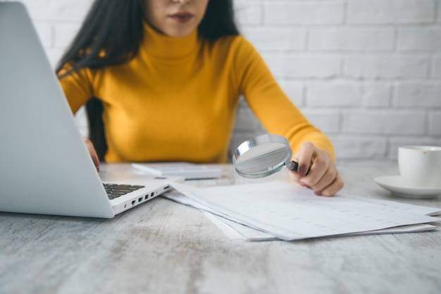 A person sitting at a desk, reviewing documents with a magnifying glass, representing the thorough auditing and compliance checks required for insurance plans.