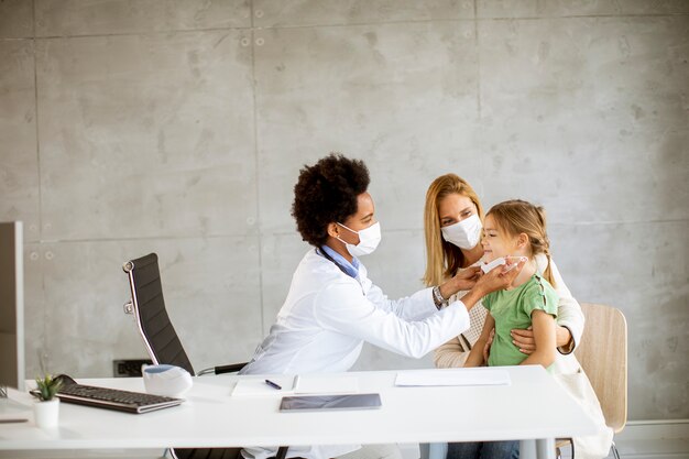 A doctor in a white coat examining a young child with a stethoscope, while the child's parent looks on with a reassuring smile. The setting is a clean and modern doctor's office.