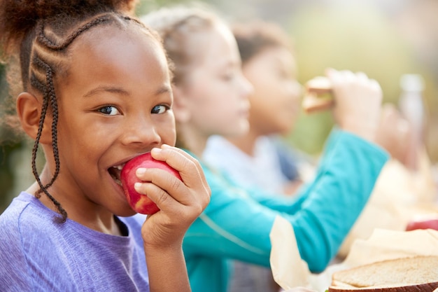 A close-up shot of a diverse group of children happily eating healthy snacks, like apple slices and yogurt. The background subtly displays the WIC logo and educational materials, reinforcing the program's focus on childhood nutrition.