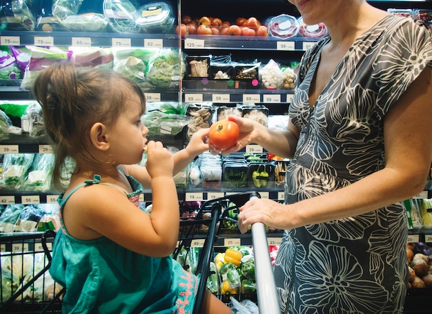 A WIC participant shopping in a grocery store with her child. She is carefully selecting WIC-approved items, holding a WIC shopping guide in her hand. The aisle is filled with colorful and nutritious foods.