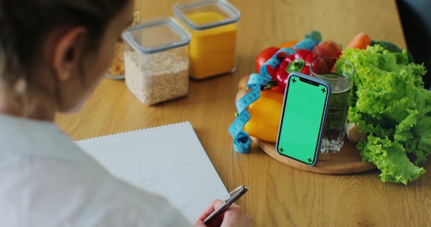 A person using a budgeting app on their smartphone while sitting at a kitchen table, surrounded by fresh groceries. The app displays a detailed breakdown of expenses and remaining SNAP balance.