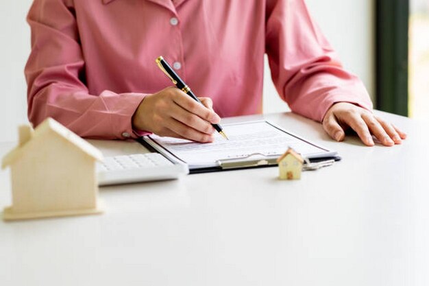 A close-up of hands filling out a housing assistance application form, with a pen and various supporting documents scattered on the table.